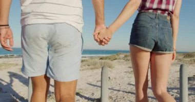 Genç beyaz bir erkek ve kadının deniz kenarında güneşli bir plajda el ele tutuşup eğlendikleri arka manzara.