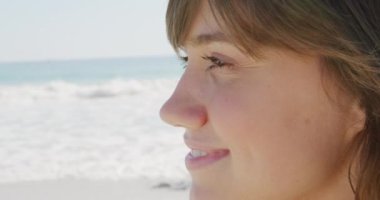 Deniz kenarında güneşli bir sahilde eğlenen, gülümseyen beyaz bir kadının yan görüntüsü.