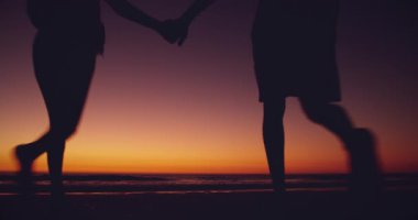 Gölgeli genç bir çiftin gün batımında deniz kenarında boş zamanlarının tadını çıkarırken görüntüsü.