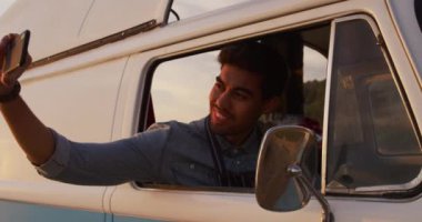 Bir yemek kamyonunun önünde oturan, selfie çeken, ağır çekimde gülümseyen melez bir ırkın ön görüntüsü.