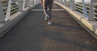 Uzun siyah saçlı, spor giyimli, şehirde egzersiz yapan, köprüde ağır çekimde koşan beyaz bir kadının arka görüntüsü..