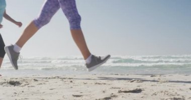 Güneşli bir günde deniz kenarında boş vakit geçiren, ağır çekimde koşu yapan bir grup beyaz kadın arkadaşın yan görüntüsü.