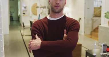 Modern bir ofiste çalışan, kollarını kavuşturmuş kameraya gülümseyen, kısa saçlı, mutlu bir beyaz iş adamının portresi..