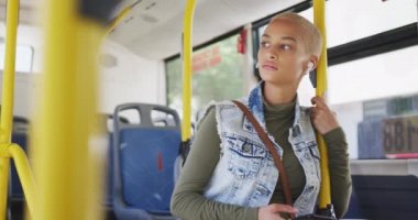 Güneşli bir günde şehirde, kısa boyalı sarı saçlı, mutlu bir melez kadının, bir otobüsün üzerinde, kulaklıkları açık bir şekilde, ağır çekimde, akıllı telefonuyla müzik dinlerken,.