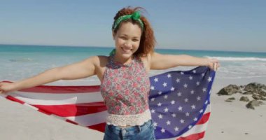 Kafkasyalı genç bir kadının güneşli bir sahilde Amerikan bayrağıyla dans edişinin ön görüntüsü.