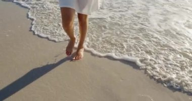 Deniz kenarında güneşli bir plajda yürüyen genç, melez bir kadının ön tarafı.