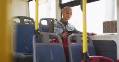 Güneşli bir günde şehirde gezen, kısa boyalı sarı saçlı, mutlu melez bir kadın otobüste oturmuş akıllı telefonunu yavaş çekimde kullanıyordu..