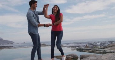 Güneşli bir günde doğada boş zamanların tadını çıkaran melez bir çiftin yan görüntüsü. Yavaş çekimde kumsalda dans ediyorlar.