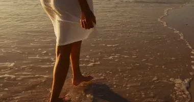 Gün batımında sahilde yürüyen genç bir melez kadının arka görüntüsü.