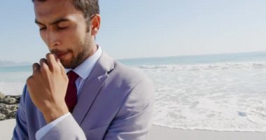 Deniz kıyısındaki güneşli bir sahilde boş vakit geçiren melez bir işadamının ön görüntüsü.