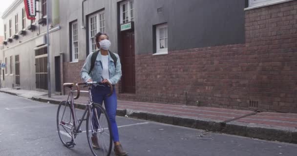 一位黑头发的混血儿站在城市街道上 头戴防空气污染面罩 头戴头罩 骑着自行车 背景为慢动作 站在一旁观看 — 图库视频影像