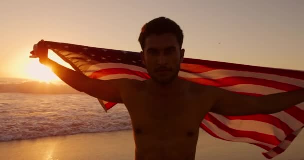 夕暮れ時にアメリカ国旗を掲揚し ビーチで自由時間を楽しむ若い混合レースマンのフロントビュー — ストック動画