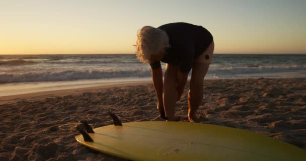 日落时分 一位白种人老妇人站在沙滩上 站在海边的沙滩上 慢吞吞地冲浪后从腿上挣脱绳子的侧影 — 图库视频影像