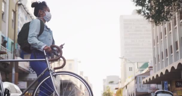 混血儿 白天留着长长的黑发 在城市街道上走来走去 戴着防空气污染的面罩 头戴头罩 骑着自行车 用智能手机 背景是慢动作的建筑物 — 图库视频影像