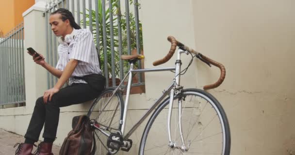 スマートフォンを使用して 彼の自転車が遅い動きで彼の隣の壁にもたれて 通りに座って 笑みを浮かべて — ストック動画
