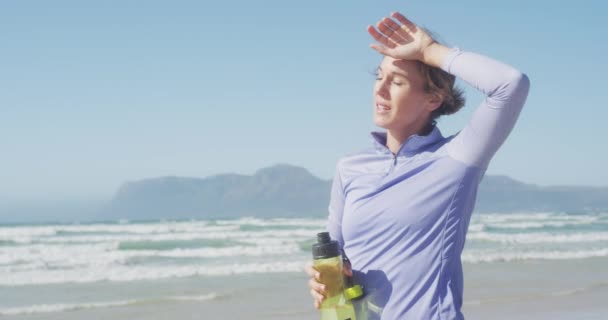 在阳光明媚的日子里 一位白人妇女在海边享受着闲暇时光 从运动中休息一下 慢吞吞地拿着一个塑料瓶 — 图库视频影像