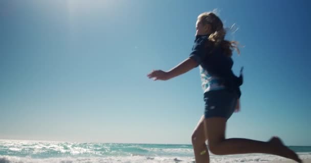 一个白人女孩在阳光灿烂的海滩上 在沙滩上跑来跑去 在沙滩上跳跃 背景是蓝天和大海 动作缓慢的后视镜 — 图库视频影像