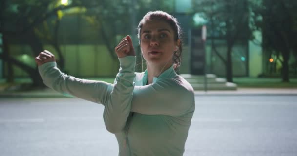 一位身材匀称 身穿运动服 夜间在城市室外锻炼 戴耳机 张开双臂的高加索女人的前视镜 — 图库视频影像