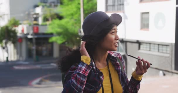 日中は街中を歩き帽子をかぶってチェックしたシャツを着てゆっくりとした動きの中で建物を背景にスマートフォンで話していました — ストック動画