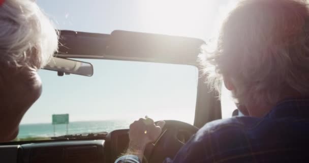 道路の旅行中に車の中で座っているシニア白人のカップルの後部のビューを閉じる 太陽の下でビーチに運転 スローモーションで車輪の男 — ストック動画