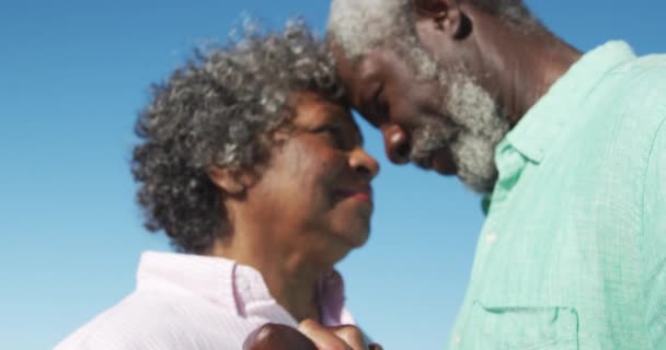 青い空を背景に 手を取り ダンスをし スローモーションで楽しみながらビーチに立っているアフリカ系アメリカ人のカップルの近くの低角度側のビュー — ストック動画