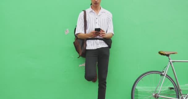 スマートフォンを使用して 通りに立って 彼の自転車は遅い動きで彼の隣の壁にもたれている — ストック動画