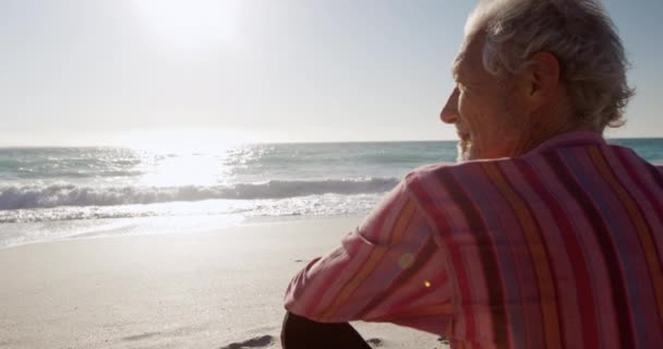 后视镜近视 一位年迈的白人男子坐在沙滩上晒太阳 坐在沙滩上 慢吞吞地望着大海 — 图库视频影像