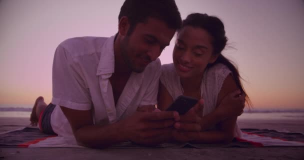 若い混合レースのカップルのフロントビュー日没時に海でビーチで自撮りを楽しむ無料の時間 — ストック動画