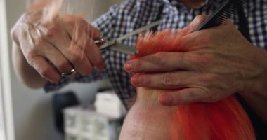 Alternatif havalı kuaför salonu. Kafkasyalı bir erkek kuaförün, elinde tarak, kesme, tarama ve okşama gibi ağır çekimde beyaz bir kadın müşterinin kızıl saçlarını ön planda tutarken görüntüsü.