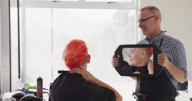 Alternatif havalı kuaför salonu. Kafkas erkek kuaförünün bir kuaförde çalışmasını beyaz bir kadın müşteriye ayna tutmasını, saç kesimini yavaş çekimde beğenmesini.