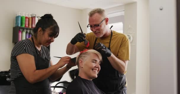 代替クールなヘアサロン 白人男性のサイドビューと混合レースの女性の美容師は ヘアサロンで作業し ブラシを保持し スローモーションで白人女性クライアントの髪の色 — ストック動画