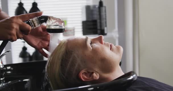 替代凉爽发廊 一个白人女性顾客在美发厅里的侧影 一个混血的女性美发师在美发厅里慢动作地洗头 — 图库视频影像