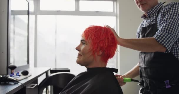 替代凉爽发廊 在一家美发店工作的白人男性美发师 拿着吹风机 慢动作地擦干和抚摸着一位快乐的白人女性客户的红头发的侧影 — 图库视频影像
