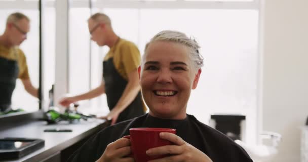 代替クールなヘアサロン 髪のサロンに座っている白人女性の顧客の肖像 コーヒーを飲みながら 背景に白人男性の美容師と スローモーションで — ストック動画