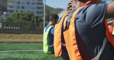 Yan görüş, spor giyim ve renkli önlük giyen, spor sahasında antrenman yapan, arka arkaya ağır çekimde mekik çeken çok ırklı erkek futbol oyuncularından oluşan bir grup.