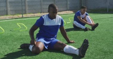 İki melez erkek futbolcunun takım elbiseli, güneşin altında antrenman yapan ısınan, esneyen, ağır çekim