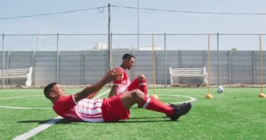 Takım elbiseli, spor sahasında antrenman yapan, mekik çeken, ağır çekimde koşan çok ırklı erkek futbolcuların yan görüntüsü.