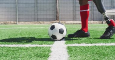 Yan görünüşte, protez bacaklı, takım elbiseli, bacağı ağır çekimde topun üzerinde duran, spor sahasında antrenman yapan karışık ırktan erkek bir futbolcunun düşük kesimi.