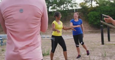 Acemi birliğinde antrenman yapan, gülümseyen ve yavaş çekimde beşlik çakan mutlu çok ırklı kadın arkadaş grubunun yan görüntüsü.