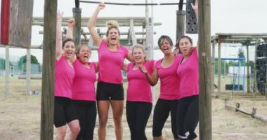 Pembe t-shirtler giyen, kampta birlikte egzersiz yapan, kucaklaşan, zıplayan ve tezahürat yapan, antrenmandan sonra kollarını kaldırarak gülümseyen mutlu çoklu etnik arkadaş grubunun ön görüntüsü.