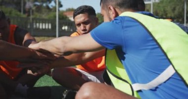 Spor kıyafetleri ve renkli önlükler giyen, spor sahasında antrenman yapan, ağır çekimde el işi yapan çok ırklı erkek futbol oyuncularının ön görüntüsü.