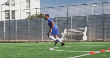 Melez bir erkek futbolcunun takım elbiseli, güneşin altında antrenman yapan, topa vuran, ağır çekimde...
