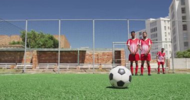 İki çok ırklı erkek futbol takımının ön görüntüsü. Takım elbiseli, güneşin altında bir spor sahasında antrenman yapan, serbest vuruş yapan, gol atan, ağır çekimde...