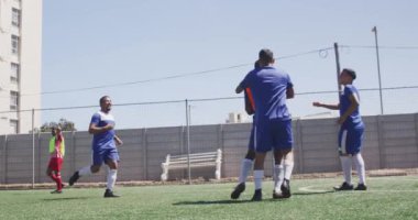 Çok ırklı iki erkek futbol takımının yan görüntüsü. Takım elbiseli, güneşin altında bir spor sahasında antrenman yapan, bir maç yapan, ağır çekimde pas veren iki erkek futbolcu.