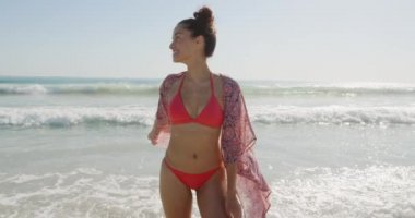 Deniz kenarında güneşli bir sahilde dans eden genç bir melez kadının ön görüntüsü.