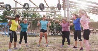 Acemi birliğinde egzersiz yapmaktan zevk alan, omuzlarında tahta direklerle çömelmiş bir şekilde, ağır çekimde çömelen mutlu çoklu etnik arkadaş grubunun ön görüntüsü.