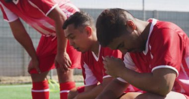 Takım elbiseli, spor sahasında antrenman yapan ve ağır çekimde dinlenen çok ırklı erkek futbolcuların yan görüntüsü.