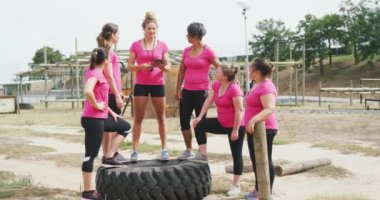 Acemi birliğindeki beyaz kadın koçun portresi. Elinde bir pano var. Hepsi de ağır çekimde pembe tişörtler giyen çok ırklı bir arkadaş grubuyla kameraya bakıyor.