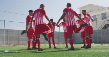 Çok ırklı erkek futbolcuların takım elbiseli, güneşin altında spor salonunda antrenman yapan, bacaklarını tek ayak üzerinde dengeleyen, ağır çekimde