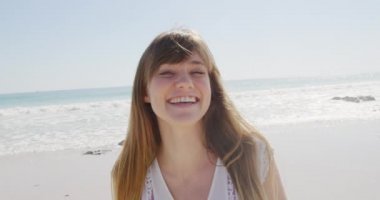 Deniz kenarında güneşli bir sahilde boş vakit geçiren, kameraya gülümseyen beyaz bir kadının portresi.